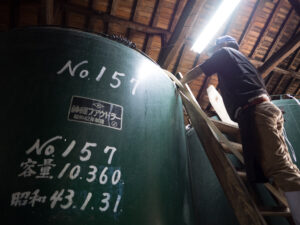 Brewery worker checking a large sake fermentation tank at Mitsutake Sake Brewery
