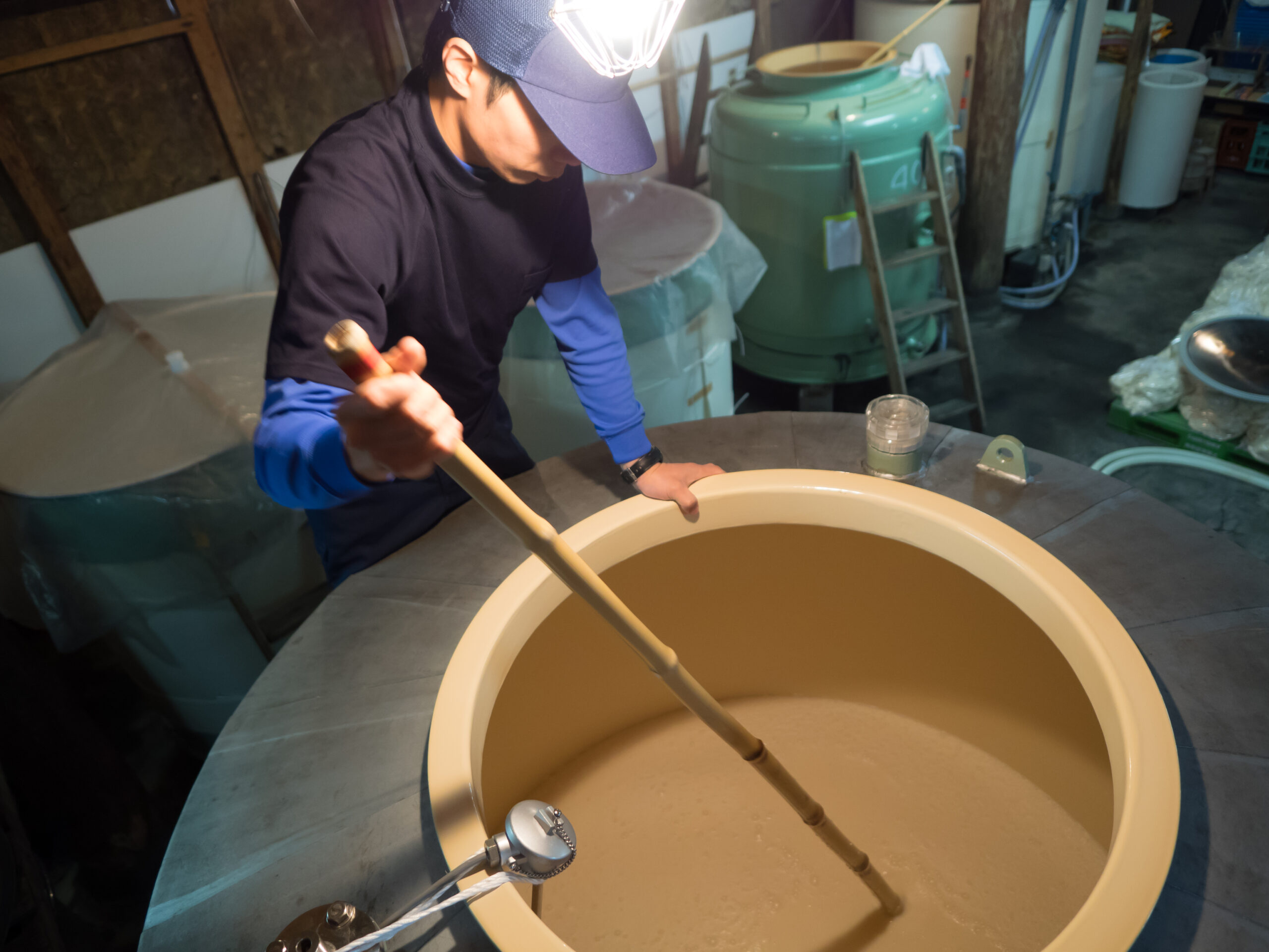 Brewer stirring moromi mash during sake fermentation at Mitsutake Brewery